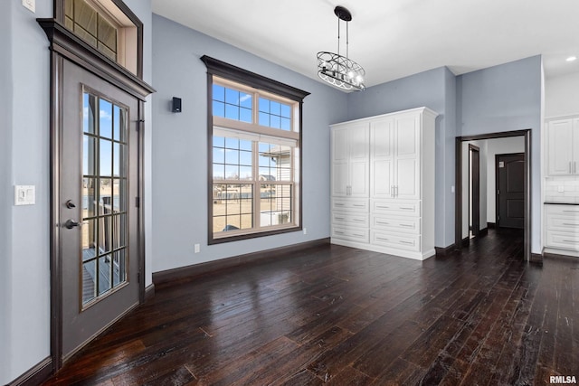 unfurnished bedroom with baseboards, a notable chandelier, dark wood-type flooring, and a closet