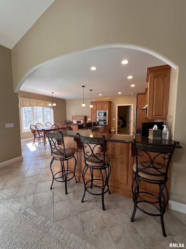 kitchen with stainless steel appliances, a breakfast bar, a peninsula, brown cabinetry, and dark countertops