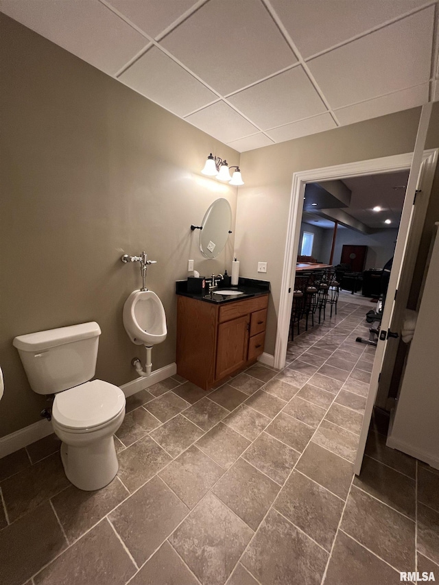 bathroom with a drop ceiling, vanity, toilet, and baseboards