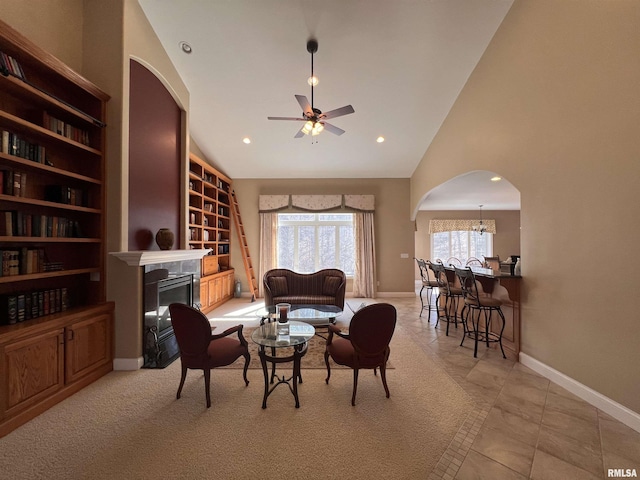 living area featuring arched walkways, high vaulted ceiling, ceiling fan, baseboards, and a glass covered fireplace