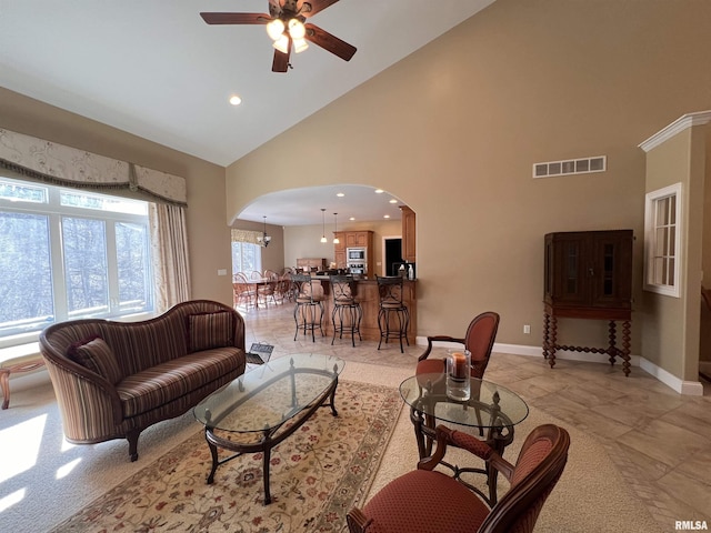 living area featuring arched walkways, visible vents, ceiling fan, high vaulted ceiling, and baseboards