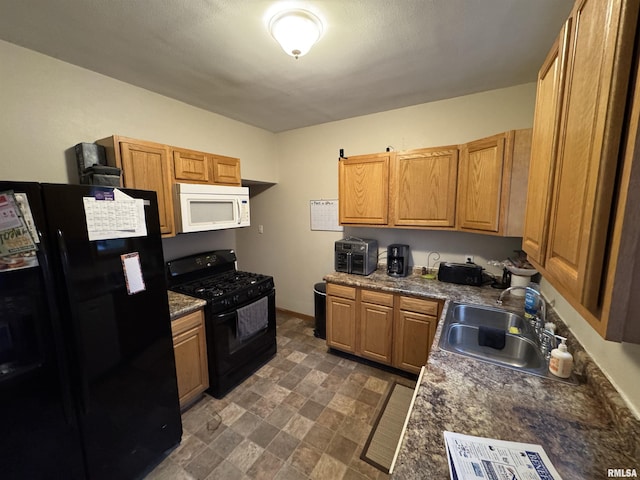 kitchen featuring dark countertops, stone finish flooring, a sink, and black appliances