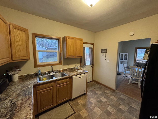 kitchen featuring dark countertops, freestanding refrigerator, white dishwasher, a sink, and baseboards