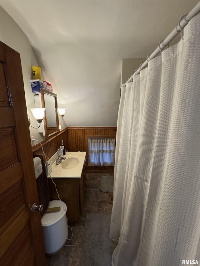 bathroom featuring wainscoting, vaulted ceiling, wood walls, vanity, and tile patterned floors