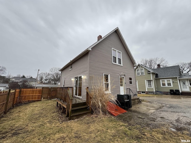 rear view of property featuring a chimney, fence, and a wooden deck