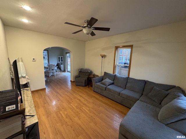 living room featuring light wood-type flooring, arched walkways, and ceiling fan