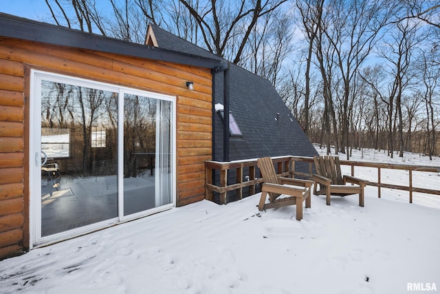 snow covered rear of property with a shingled roof and log veneer siding
