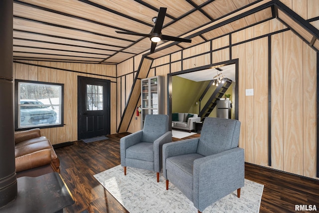 living area featuring wood walls, dark wood finished floors, and ceiling fan with notable chandelier