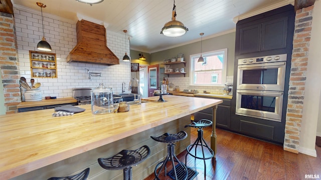 kitchen featuring double oven, butcher block countertops, crown molding, and premium range hood