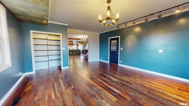 unfurnished dining area featuring wood-type flooring, crown molding, baseboards, and an inviting chandelier