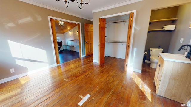 unfurnished bedroom featuring baseboards, hardwood / wood-style floors, a sink, crown molding, and a notable chandelier