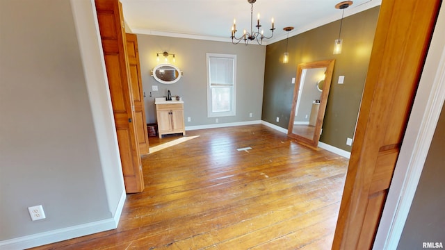 unfurnished dining area with baseboards, ornamental molding, a sink, light wood-style floors, and a notable chandelier