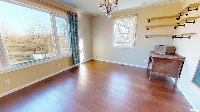 unfurnished room with a notable chandelier, visible vents, ornamental molding, wood finished floors, and baseboards