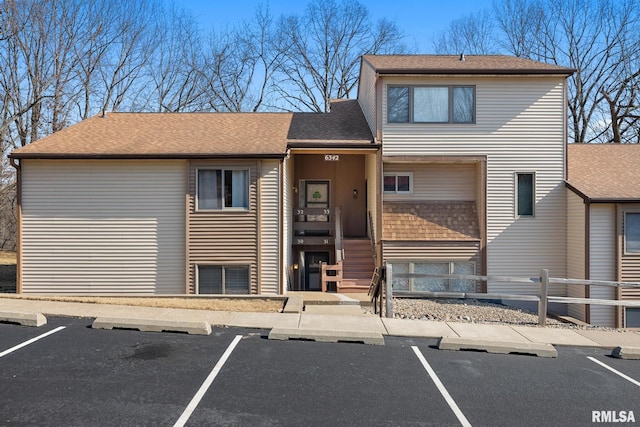 view of front facade featuring uncovered parking, a shingled roof, and fence