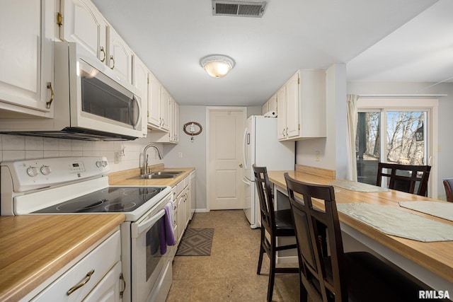 kitchen with white appliances, a sink, white cabinetry, visible vents, and decorative backsplash