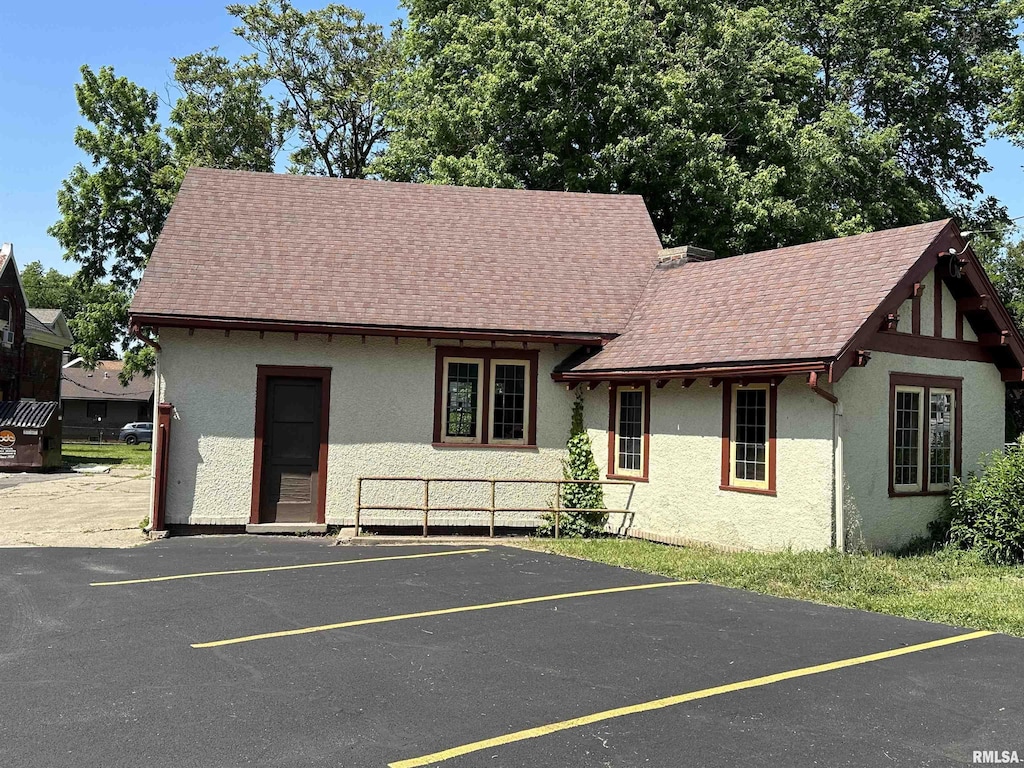 view of front of property featuring roof with shingles, uncovered parking, and stucco siding