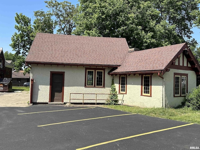 view of front of property featuring roof with shingles, uncovered parking, and stucco siding