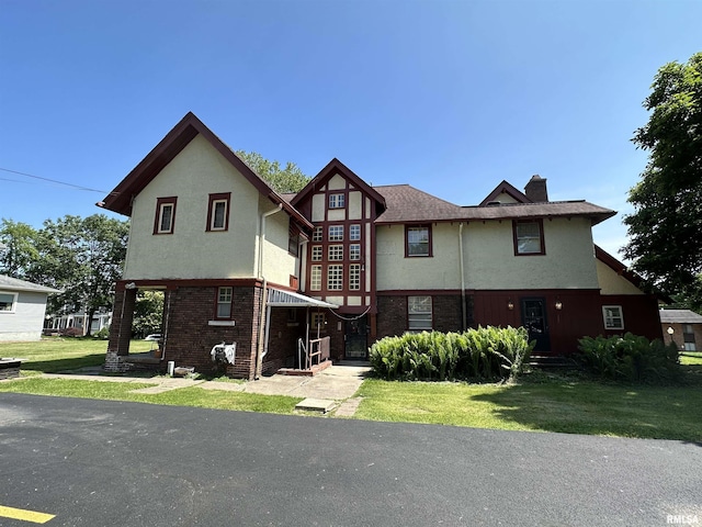 tudor home with a front yard, brick siding, and stucco siding