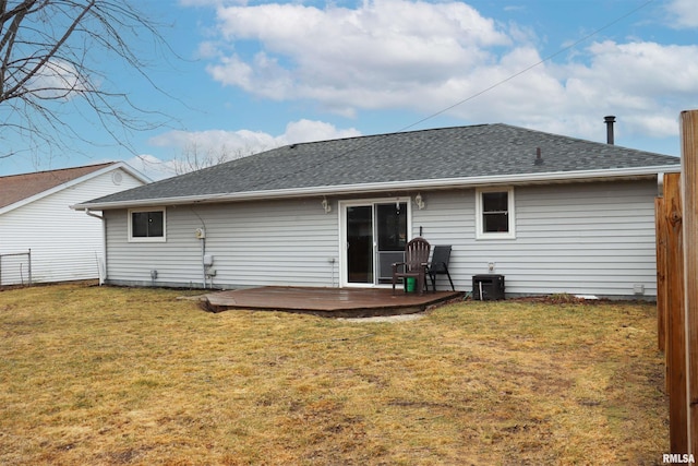 rear view of house with a shingled roof, a lawn, a deck, and fence