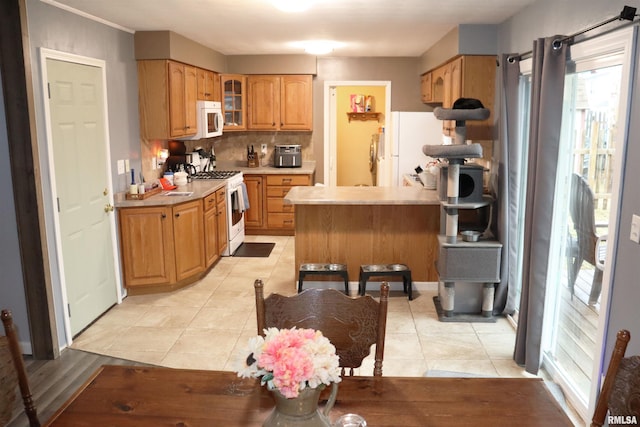 kitchen with light tile patterned floors, light countertops, backsplash, glass insert cabinets, and white appliances