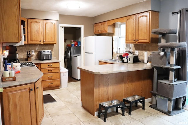 kitchen featuring washing machine and dryer, a peninsula, a sink, freestanding refrigerator, and decorative backsplash