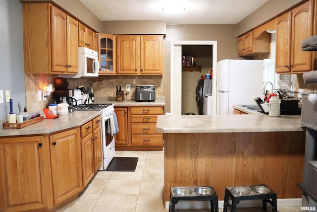 kitchen featuring light tile patterned floors, decorative backsplash, glass insert cabinets, white appliances, and a peninsula