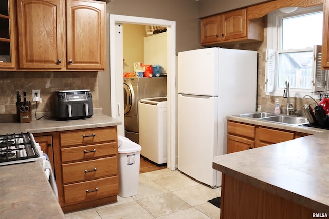 kitchen featuring a sink, freestanding refrigerator, tasteful backsplash, brown cabinetry, and washing machine and clothes dryer