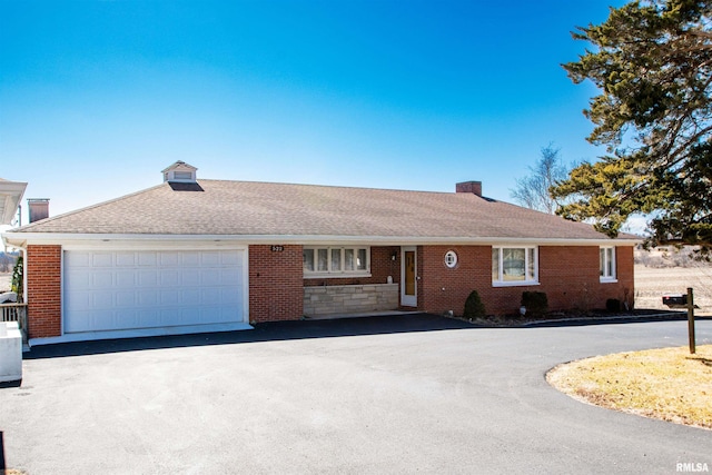 single story home featuring driveway, brick siding, a chimney, and an attached garage