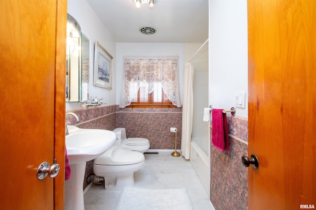 bathroom featuring toilet, visible vents, tile walls, wainscoting, and shower / bath combo with shower curtain