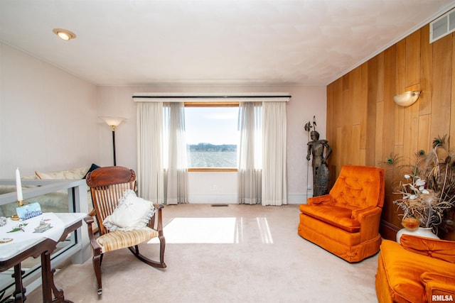 sitting room with carpet floors, visible vents, and wooden walls