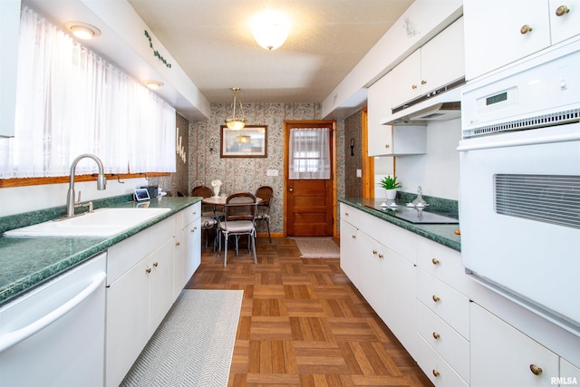 kitchen with white cabinets, a sink, white appliances, under cabinet range hood, and wallpapered walls