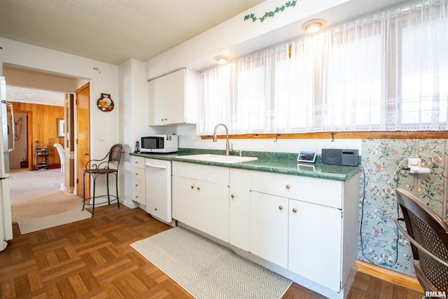 kitchen with dark countertops, white microwave, white cabinets, a sink, and wooden walls