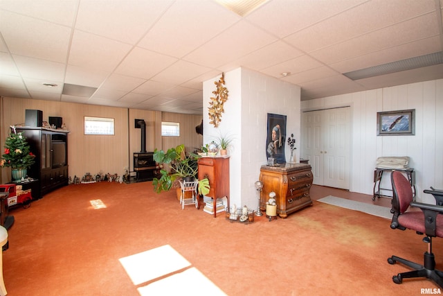 interior space with a wood stove, carpet, and a drop ceiling