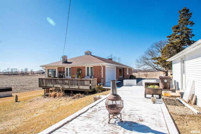 rear view of house featuring an outdoor fire pit, brick siding, an attached garage, and a wooden deck