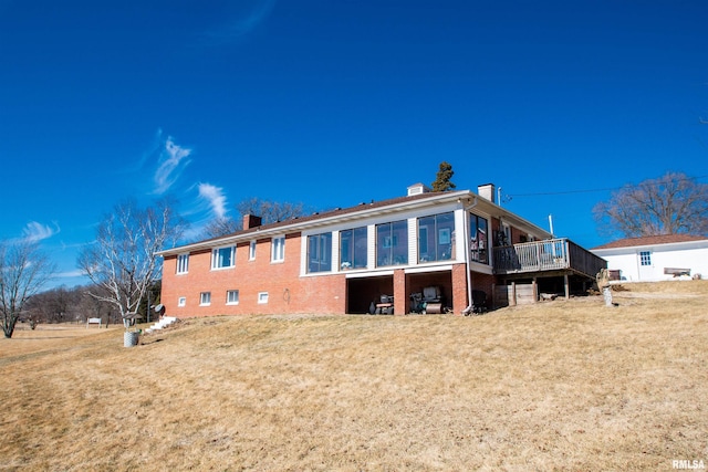 rear view of house featuring a yard, a wooden deck, a chimney, and brick siding