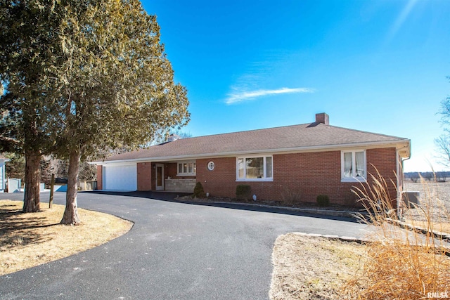 ranch-style house with a garage, brick siding, driveway, roof with shingles, and a chimney