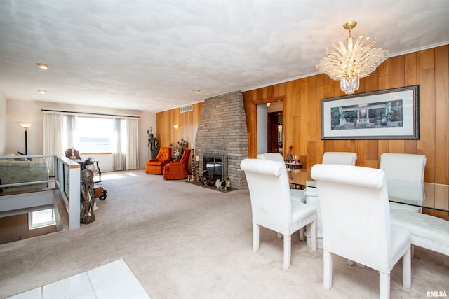 carpeted dining room featuring a notable chandelier, a brick fireplace, visible vents, and wooden walls