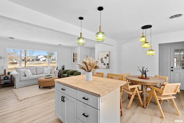 kitchen featuring a center island, light wood finished floors, hanging light fixtures, white cabinets, and wood counters