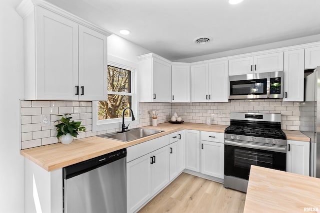 kitchen with stainless steel appliances, a sink, wooden counters, and white cabinetry