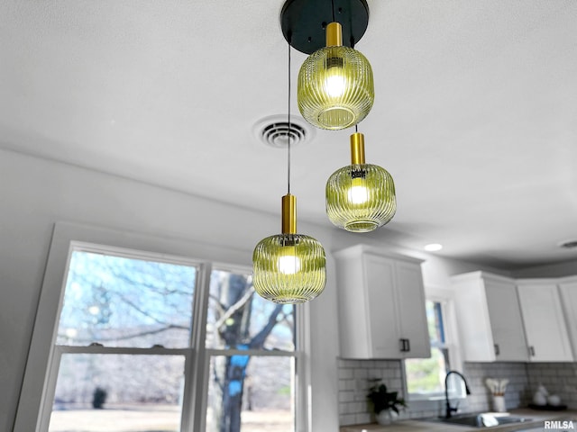 interior details with pendant lighting, tasteful backsplash, visible vents, white cabinets, and a sink