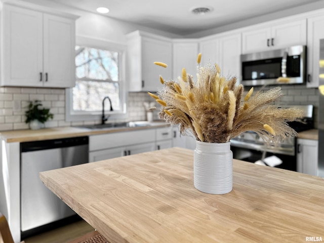 kitchen featuring white cabinets, decorative backsplash, stainless steel appliances, and a sink