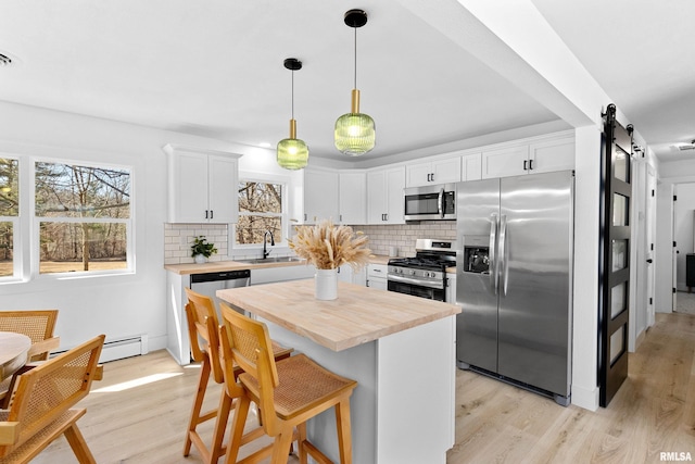 kitchen with a barn door, white cabinets, butcher block countertops, appliances with stainless steel finishes, and a sink