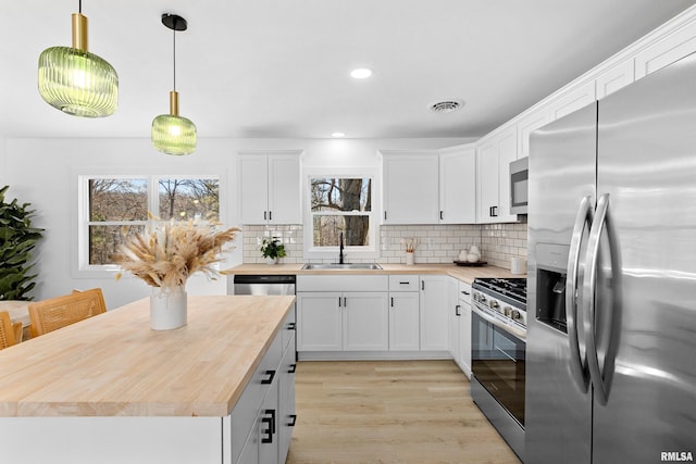 kitchen with stainless steel appliances, butcher block counters, a sink, visible vents, and backsplash