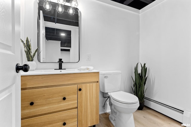 half bath with toilet, baseboard heating, vanity, wood finished floors, and baseboards