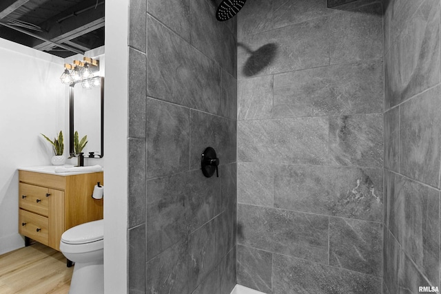 bathroom with toilet, vanity, wood finished floors, and tiled shower