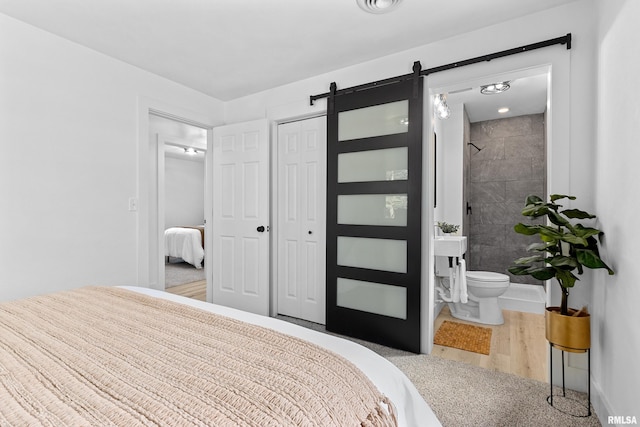 bedroom featuring a closet, wood finished floors, connected bathroom, and a barn door