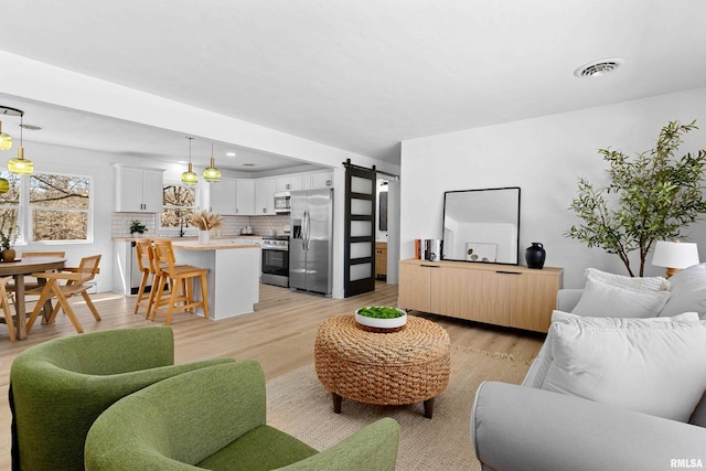 living area with visible vents, light wood finished floors, and a barn door