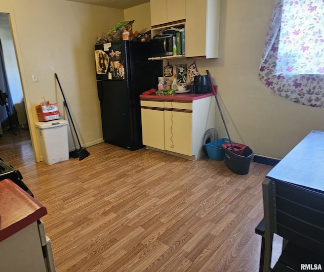 kitchen featuring light wood finished floors, stainless steel microwave, freestanding refrigerator, white cabinets, and baseboards