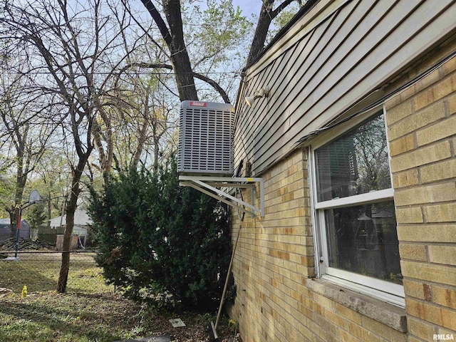 view of side of property featuring brick siding, cooling unit, and fence