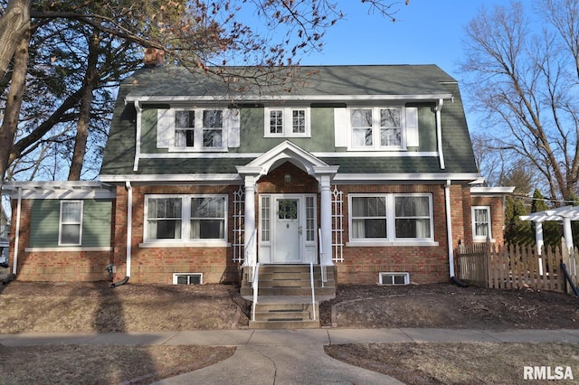 dutch colonial featuring a shingled roof, brick siding, and fence